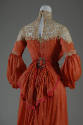 Back view of red-orange dress showing keyhole back, cream lace trim above elbow and square meta…