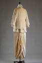 Back view of beige velvet hip length jacket, lace collar and matching floor length draped skirt