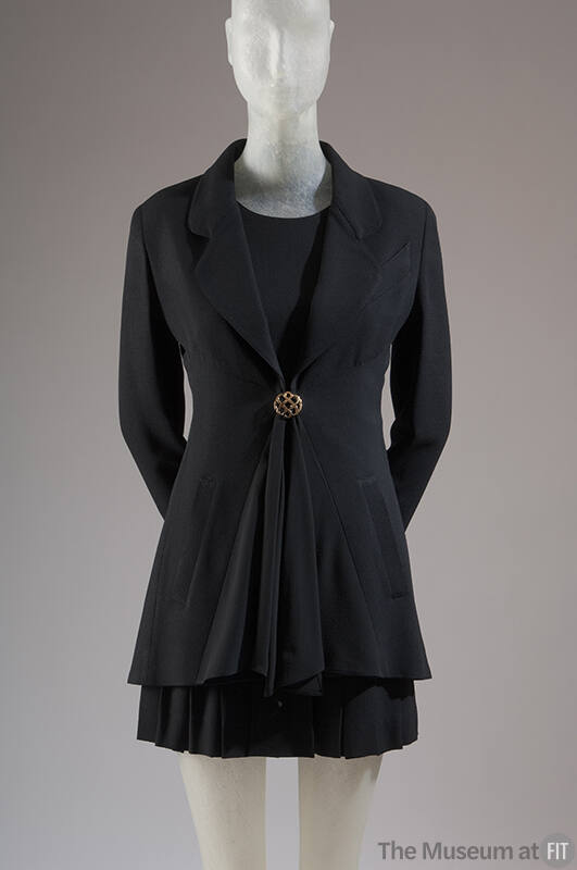 Black long sleeve jacket with peplum front and single brass button, matching pleated mini skirt