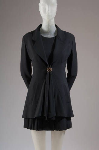 Black long sleeve jacket with peplum front and single brass button, matching pleated mini skirt