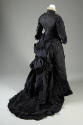 Back view of two-piece blue/grey dress showing rouched sleeves, rouched ruffle and tassel trim …