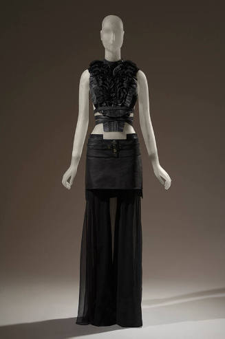 Black leather pleated top with black ruffled bib front and crisscross leather straps at waist, …
