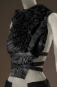 Detail of black leather pleated top with black ruffled bib front and crisscross leather straps …