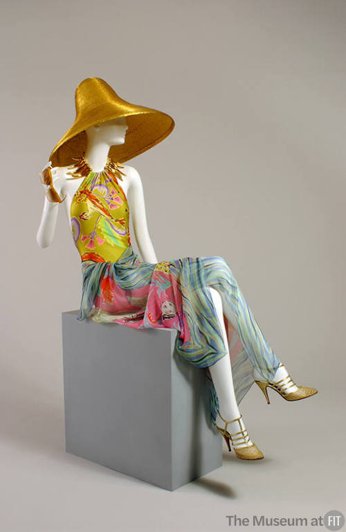 Gold straw sun hat, yellow floral bathing suit, blue multicolor sarong, gold strappy high heel …