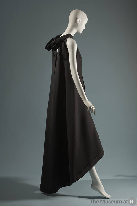 Side view of sleeveless flared black evening dress with bias roll collar tied into a large bow …