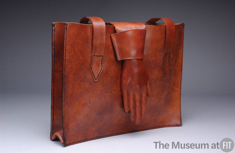 Rectangular brown/red leather tote bag with large molded hand with a shirt cuff extending down …
