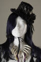 Detail view of mannequin face wearing a long blue wig showing black lace hat with chain and cro…