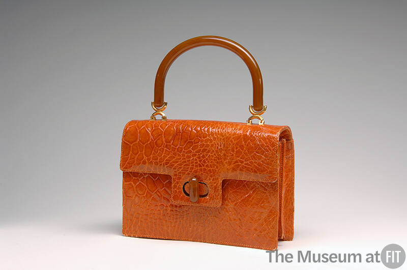 Orange alligator envelope bag with amber top handle attached by gold rings and tab flap closure…