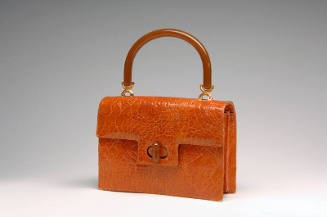 Orange alligator envelope bag with amber top handle attached by gold rings and tab flap closure…
