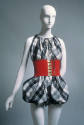 Sleeveless black and white plaid romper with puffed legs, dressed with wide red cinch belt with…
