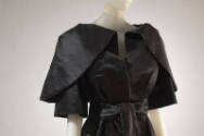 Black cape with large putt sleeves that fold over the shoulder, matching waist sash