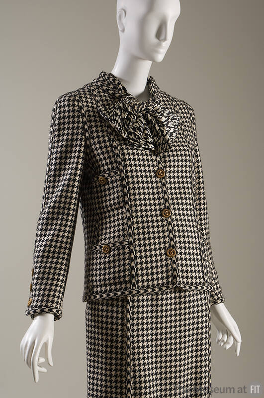 Black and white houndstooth suit with large bow at neck, four patch pockets and large gold butt…