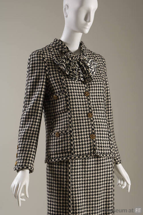 Black and white houndstooth suit with large bow at neck, four patch pockets and large gold butt…