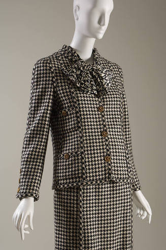 Black and white houndstooth suit with large bow at neck, four patch pockets and large gold butt…