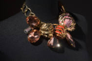 Gold chain choker necklace with orange gems and red and pink painted shells on black background