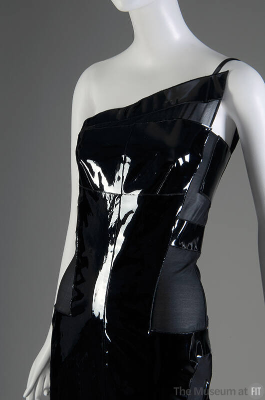 View of top half of black sleeveless one-shoulder dress with triangular patent leather panel ov…