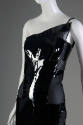 View of top half of black sleeveless one-shoulder dress with triangular patent leather panel ov…
