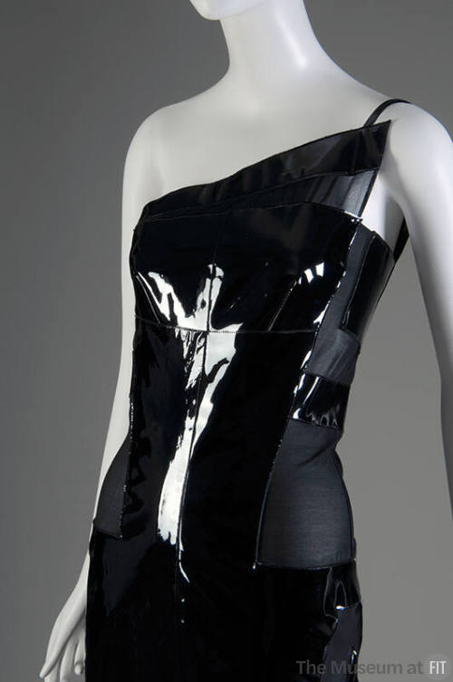 View of top half of black sleeveless one-shoulder dress with triangular patent leather panel ov…