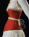 Detail view of red corset shown with white laced trimmed combination petticoat and bustle of do…