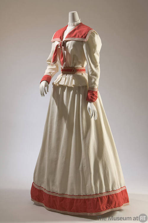 White two-piece long sleeve dress with red sailor collar, red belt and red trim around wrists a…