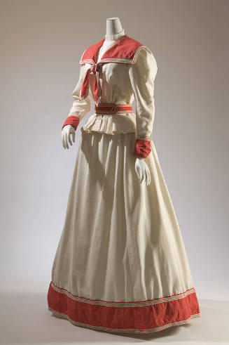 White two-piece long sleeve dress with red sailor collar, red belt and red trim around wrists a…