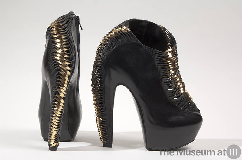 High black platform ankle boots with rows of horizontal strips twisting into gold metallic leat…