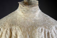 Detail view of white cotton dress showing stand collar and upper bodice made of rows of lace 