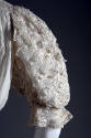 Detail view of white cotton dress showing elbow length puffed sleeves made of rows of lace 