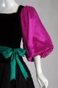 Detail view of black gown showing fuchsia balloon sleeve cinched at elbow and green belt tied w…