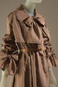 Detail of taupe rain coat with large bow at neck sleeve cuffs, tan leather belt