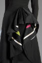 Detail view of black evening dress showing overskirt draping in pleats at hip to reveal ivory, …