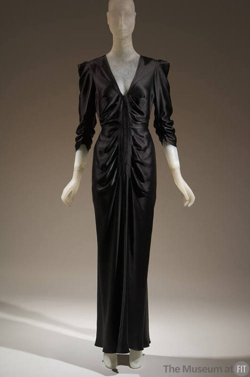Black satin floor length 3/4 sleeve dress with deep v-neck, ruching at sleeves and front bodice…