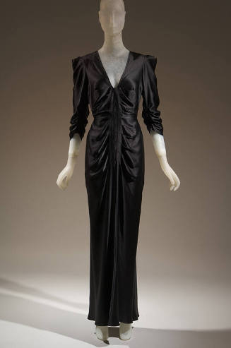 Black satin floor length 3/4 sleeve dress with deep v-neck, ruching at sleeves and front bodice…
