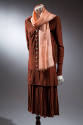Brown skirt suit with tunic-length buttoned blouse with long sleeves, loosely pleated skirt and…