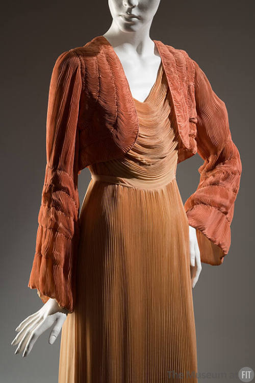 Light orange dress with cowl draped bodice of horizontally pleated fabric and vertically pleate…