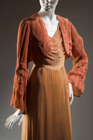 Light orange dress with cowl draped bodice of horizontally pleated fabric and vertically pleate…