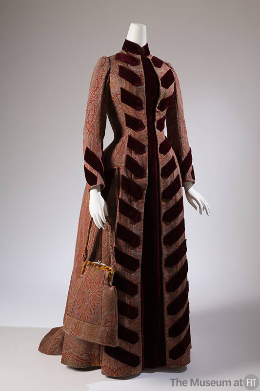 Red, tan, pink, blue, green paisley long sleeve floor length coat style dress trimmed with dark…