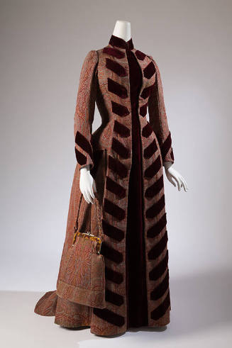 Red, tan, pink, blue, green paisley long sleeve floor length coat style dress trimmed with dark…