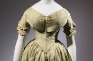 Alternate view of pale green dress without capelet showing wide V-neck of overlapping pleats an…