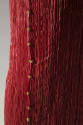 Detail view of red pleated teagown side seams showing yellow beads with red and black stripes
