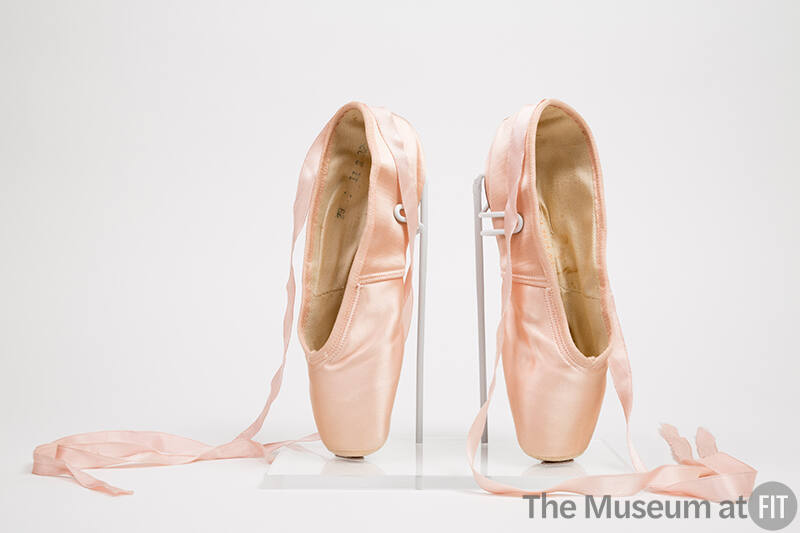 Pair of pink satin ballet pointe shoes with ankle tie ribbons, positioned upright on toe boxes