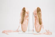 Pair of pink satin ballet pointe shoes with ankle tie ribbons, positioned upright on toe boxes