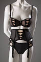 Black bra, panties, and garter belt set with faux corset lacing over beige fabric