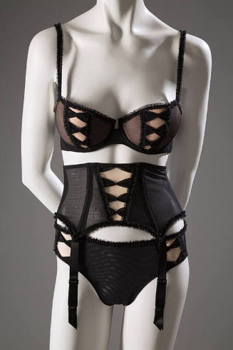 Black bra, panties, and garter belt set with faux corset lacing over beige fabric