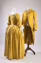 Yellow/green dress shown from the back with bustle skirt on left and man’s cutaway jacket in sa…
