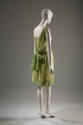 Back view of green and white sheath dress printed with leaves. Two panels drape from shoulder s…