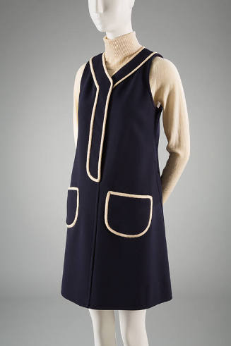 Blue jumper style dress with off-white piping at V-neck and patch pockets over off-white turtle…