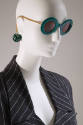 Green sunglasses with round frame and gold metal chain arms ending in green dice with grey and …