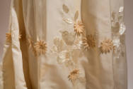 Detail view of off-white wedding gown showing silk embroidered flower and leaf motif with appli…