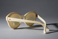 Ivory sunglasses with curved slit at eye center; gold metal studs at temples; stamped Depose an…